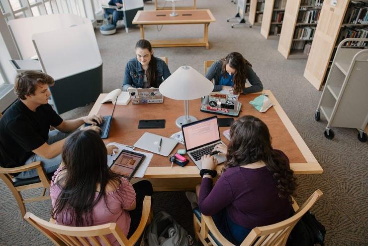 五个立博体育登录的学生围坐在图书馆的桌子旁，拿出了他们的笔记本电脑